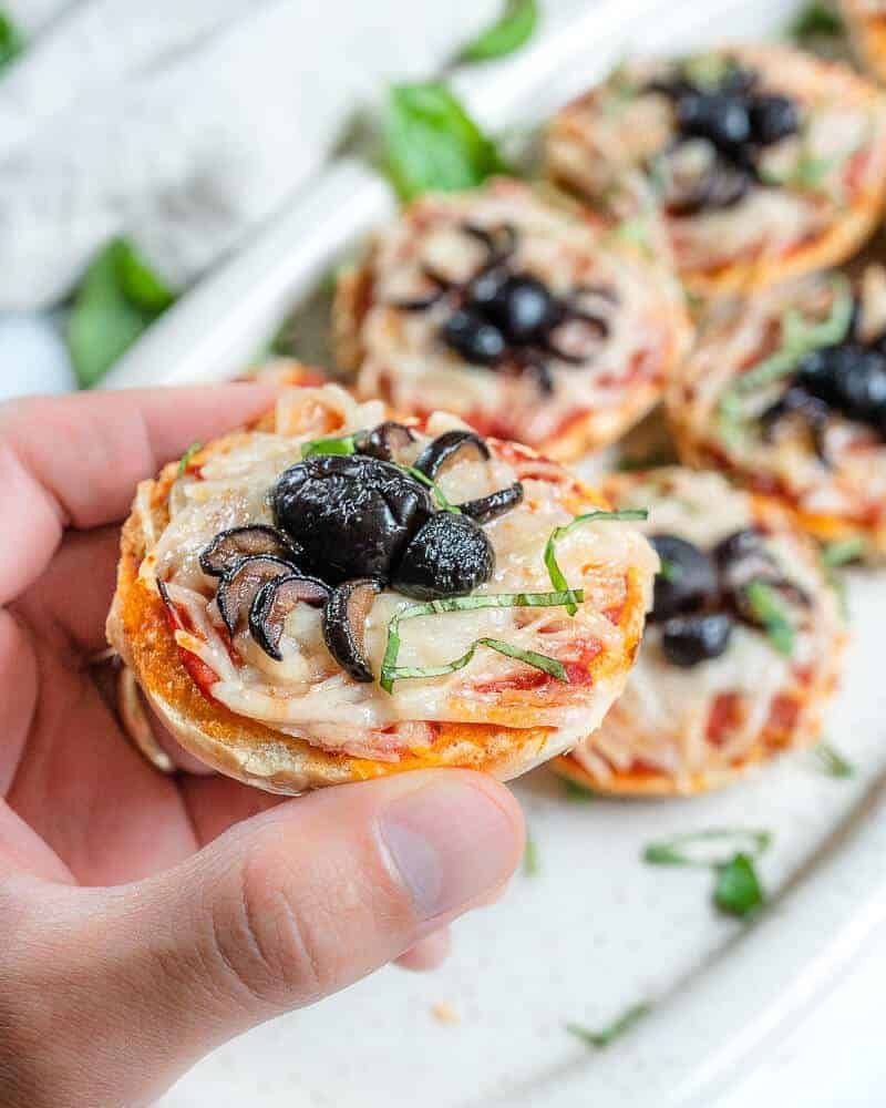 Mini bagel halves topped with cream cheese, sliced olives for eyes, and pretzel “legs” forming spiders on a black platter